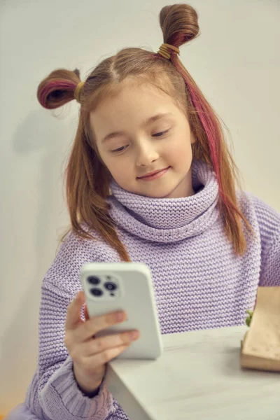 stock image Beautiful little girl with ponytails browsing mobile app on a smart phone with a smile. Cute white kid using a gadget