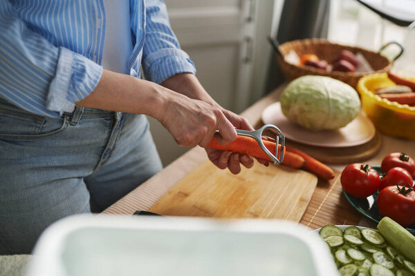 Woman peeling off a carrot for lunch. Housewife preparing vegetables for salad in the morning