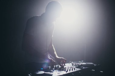 Sahnede plakları karıştıran kulüp DJ 'inin silueti. Gece kulübünde konser veren bir diskjokeyin sahne arkası.