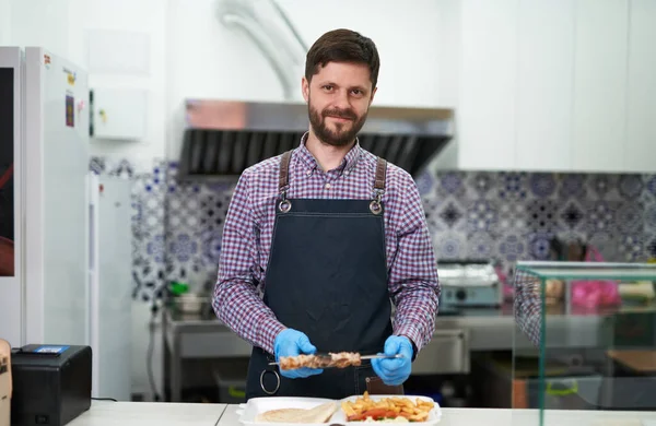一个快乐的年轻人正在煮希腊快餐 准备带走 一个快乐的店主用苏弗拉基肉和薯条做午餐盒的肖像 — 图库照片