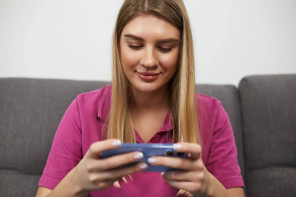 快乐的金发女青年用智能手机观看网上视频 一个漂亮的白人妇女坐在沙发上用手机的画像 — 图库照片