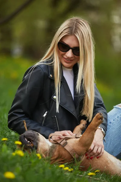 金发女子在户外和她的宠物玩耍 一个快乐的年轻女人给她的法国斗牛犬擦了一下肚子 — 图库照片