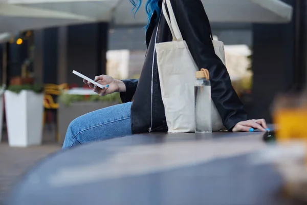 年轻女子坐在城市街道的长椅上 用智能手机 负责任的女性 提着手提包和玻璃瓶在户外浏览手机应用程序 — 图库照片
