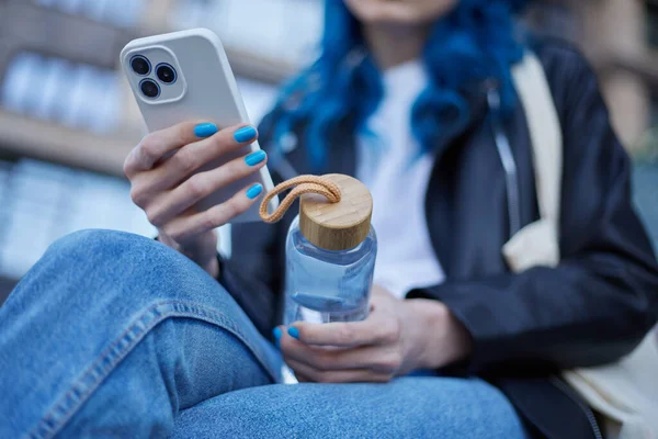 Молодая Женщина Держит Стеклянную Бутылку Воды Руках Просматривая Мобильное Приложение — стоковое фото