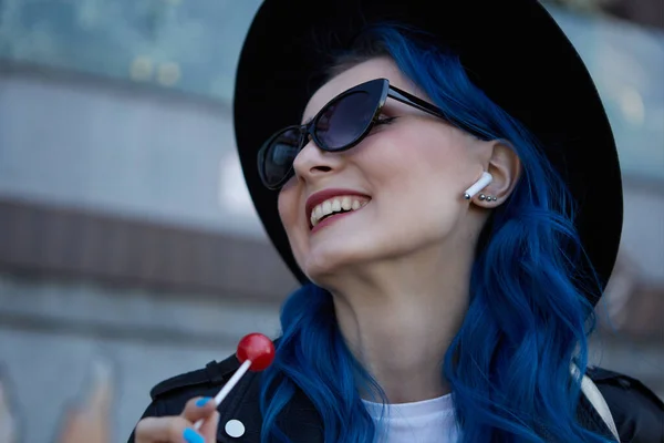 一个快乐多样的女人的画像 她的头发染成蓝色 听着音乐 吃着棒棒糖 快乐的年轻女子在无线耳机里听音乐 — 图库照片