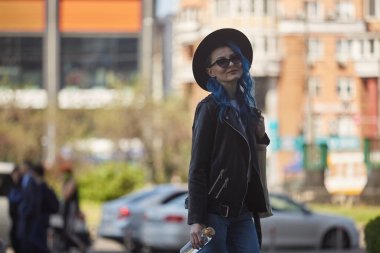 Mavi saçlı neşeli bir kadın cam bir su şişesiyle dışarıda yürüyor. Güzel beyaz bir kadının portresi şık bir hippi şapkası ve güneş gözlüğü takıyor.