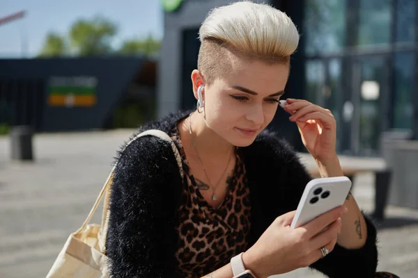 不同类型的人的肖像 短发听音乐在无线耳机连接到智能手机 外面用手机的漂亮白人女人 — 图库照片