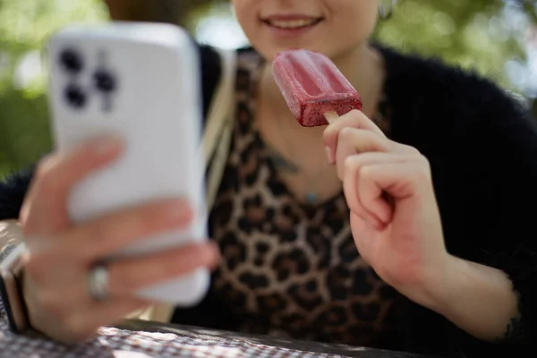 Ευτυχισμένη Νεαρή Γυναίκα Τρώει Ένα Παγωτό Και Περιήγηση Μια Εφαρμογή — Φωτογραφία Αρχείου