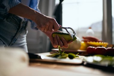 Sabahleyin bir ev mutfağında, bir salatalık soyan bir kadın. Kadın öğle yemeği için taze yeşil salata hazırlıyor.