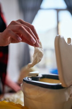 Kadın el, mayalanması için arta kalan yiyecekleri bokashi kabına atıyor. Ev hanımı organik atıkları iç gübre kutusunda geri dönüştürüyor.