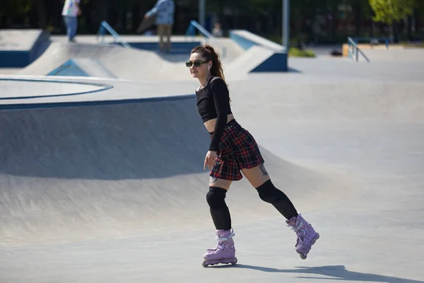 年轻可爱的成年女子骑在一个混凝土滑雪场的激进内联溜冰鞋 夏天在一个城市公园里穿格子花裙子滑冰的轮滑女 — 图库照片