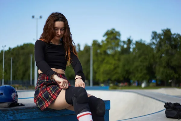 女性スケーターはスケート用の保護膝パッドをつけている 夏に都会のスケートパークに乗る準備をしている赤い髪の若い大人 — ストック写真