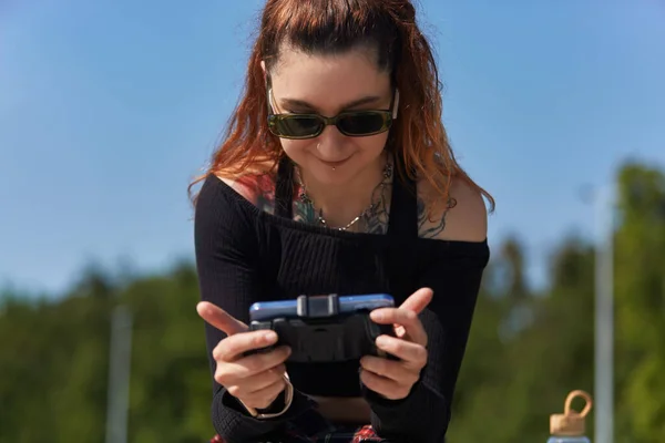 快乐的游戏玩家用智能手机和游戏面板玩手机游戏 用现代小玩意在网上玩太阳镜游戏的纹身的年轻成年女性的画像 — 图库照片