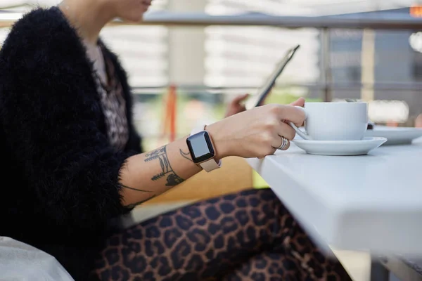 身穿豹衣的年轻女子在餐馆的阳台上喝咖啡 难以辨认的女性坐在室外咖啡馆里 午餐时在平板电脑上浏览互联网 — 图库照片