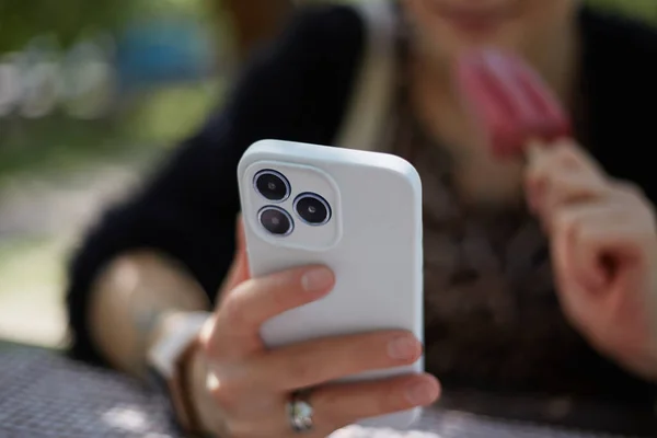 Молодая Женщина Просматривает Мобильное Приложение Современном Смартфоне Ест Мороженое Открытом — стоковое фото