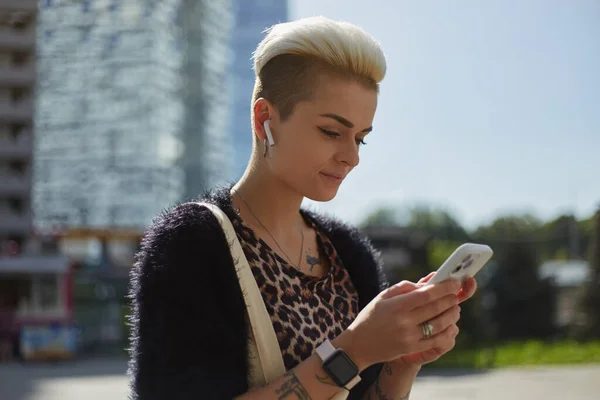 时尚多样的女人 听音乐 在户外用智能手机打字 漂亮的白人女性使用手机在网上交流 — 图库照片