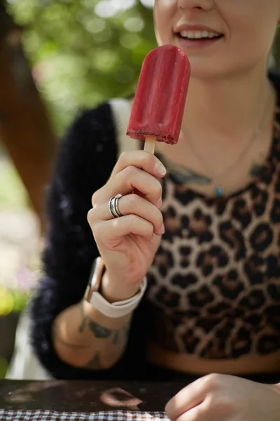 若い女性が緑の公園で赤いアイスクリームを食べている 夏のカフェに座っているヒョウの服の認識できない白い女性とクランベリーアイスクリームデザートを舐める — ストック写真