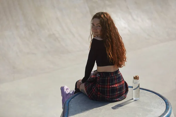 スケートプールでポーズをとる若いインラインローラーブラダー女性 水のグラスボトルでランプの上に座っているスケーターの肖像画 — ストック写真