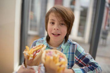 Neşeli ve aç küçük çocuk bir Yunan kafesinde sandviç yemeye hazırlanıyor. Güzel beyaz bir çocuğun portresi bir restoranda öğle yemeğinde fast food yiyor.