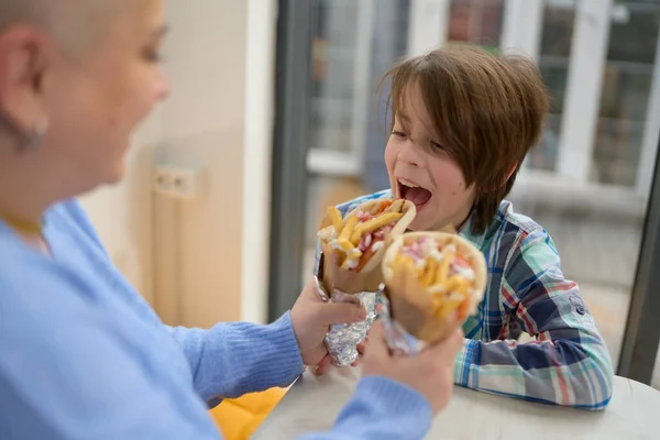 空腹の少年は カフェでサンドイッチを包んだジャイロの一口を取って 母親給餌彼女の11歳の息子で伝統的なギリシャのファーストフードでヨーロッパのレストラン — ストック写真