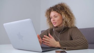 Bir konferans sırasında web kamerasında konuşan kıvırcık saçlı, arkadaş canlısı ve duygusal bir genç kadın. Kulaklık takmış neşeli beyaz kadın dizüstü bilgisayarla konuşuyor.