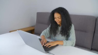 Evdeki dizüstü bilgisayarda yazı yazan neşeli siyahi kadın. Savaş esiri kadın oturma odasında modern bir defter üzerinde çalışıyor.
