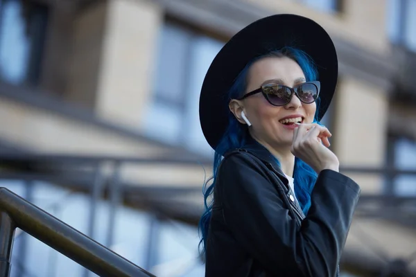 一个漂亮的年轻女子的画像 她的头发染成蓝色 手里拿着棒棒糖 头戴嬉皮士帽 身穿黑色皮衣 面带微笑站在户外的时尚而又多样化的女性 — 图库照片