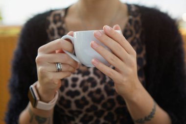 Dövmeli elleri olan genç bir kadın sabahları kahve içiyor. Tanımlanamayan bir kadın öğle yemeğinde bir fincan espresso içiyor.