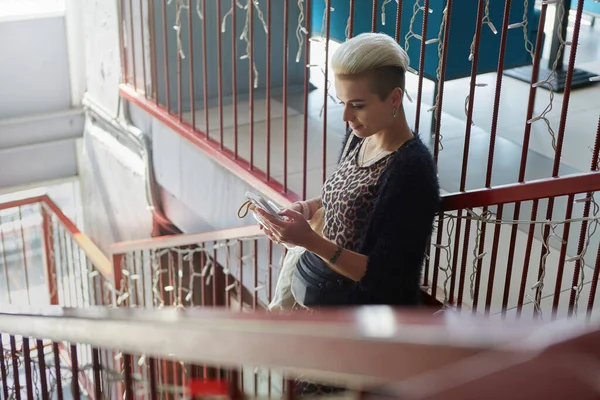 一头短发的白人妇女站在一家咖啡馆的楼梯上 浏览着一部手机 用智能手机与不同款式的豹纹女模特进行交流 — 图库照片