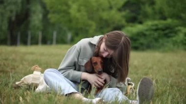 Sahibi tekerlekli sandalyede felçli köpeğe sarılıyor. Genç kız engelli evcil hayvanıyla dışarıda oynuyor.