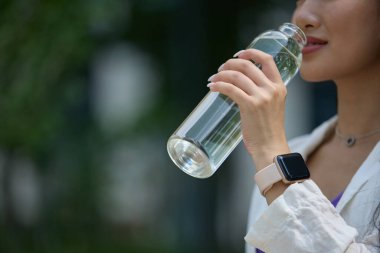 Dışarıdaki cam şişeden su içen genç Asyalı kadın. Susamış bir kadın yürüyüş yaparken bir yudum maden suyu alıyor.