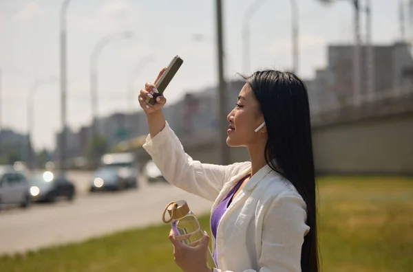 漂亮的年轻亚洲女人拿着智能手机拍照 一个年轻可爱的越南女人头戴无线耳机 手里拿着一瓶水的画像 — 图库照片