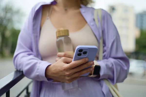 一个穿着紫色衣服的时髦的年轻女人 用的是一个穿着紫色被子的现代智能手机 难以辨认的女性在户外用新手机浏览应用程序 — 图库照片