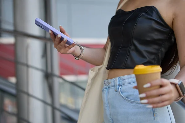 小女孩站在楼梯上 手里拿着智能手机和咖啡 一个难以辨认的女人在一个手机上浏览应用程序 在商场里散步时喝卡布奇诺 — 图库照片