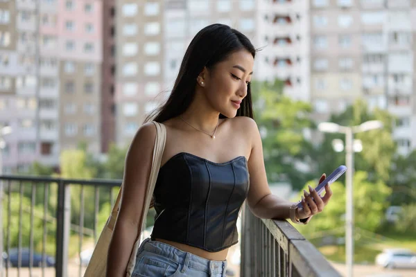 漂亮的年轻越南女性在户外阳台上使用智能手机 一个快乐的东南亚女人用现代手机浏览手机应用程序的肖像 — 图库照片
