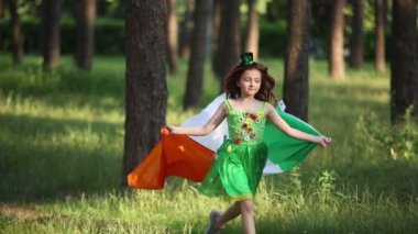 St Patricks Day celebration. Cheerful white girl in green pixie dress running in the wood with flag of Ireland in slow motion