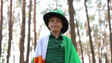 Funny little boy dressed as a leprechaun and covered with flag of Ireland. Cute kid posing for a video on St Patricks Day