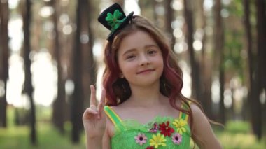 Cute leprechaun girl posing in the sunny forest. Beautiful little girl wearing green fairy dress and cylinder hat for a St Patricks Day celebration