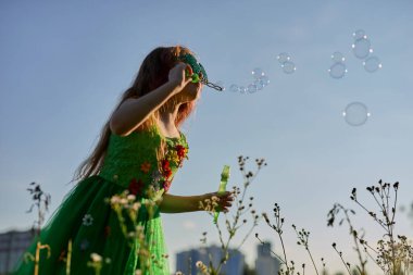 Aziz Patrick Günü 'nde yeşil peri gibi giyinmiş küçük beyaz kız baloncuklar üflüyor.