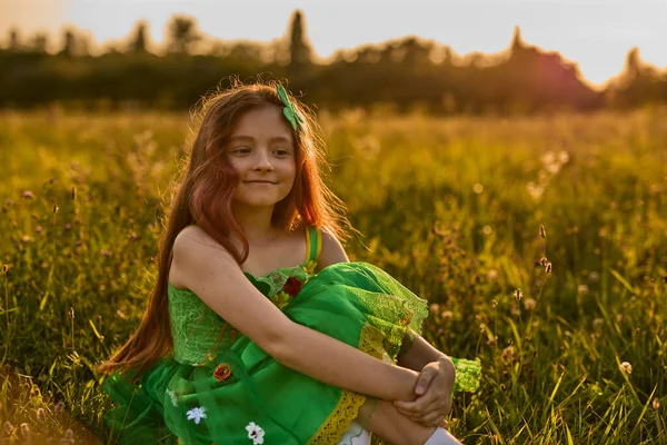 日落时穿着绿色仙女衣服的可爱的小女孩坐在田野里 美丽的红头发孩子穿上衣服参加圣帕克斯节 — 图库照片