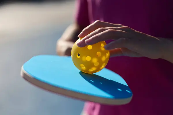 Pickle ball athlete holding a racket and a perforated plastic ball in hands