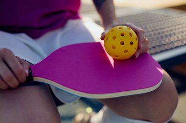 Pickleball oyuncusu elinde bir raketle sahada oturuyor.