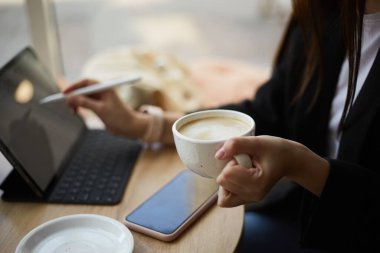 Serbest çalışan, kahve içen ve kafedeki tablet bilgisayara bir skeç çizen biri.