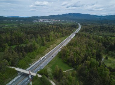 Slovenya kırsalındaki otoyol yeşil orman ağaçlarıyla çevrili, yukarıdan insansız hava aracı kamerasıyla çekilmiş.