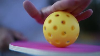 Pickleball atleti raketin üzerinde plastik bir topu yuvarlıyor.