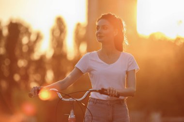 Güzel ve sağlıklı genç bir kadın gün batımında bisikletle yürüyor.