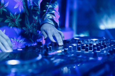 Gece kulübü DJ 'i parlak mavi ışıklarla tekno müzik çalıyor. Profesyonel disk şakası, müzik parçalarını ses karıştırıcı ile karıştırıyor