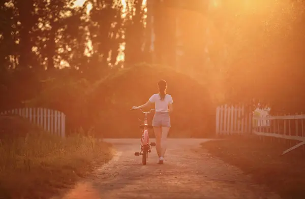 Slim young woman walking with a bike at sunset. Healthy female lifestyle
