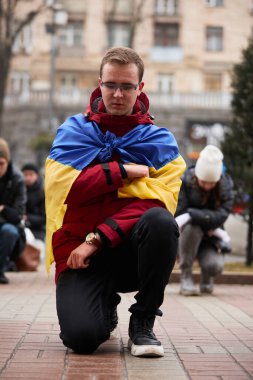 Ukraynalı vatansever, Ukrayna 'nın ulusal bayrağını omuzlarında taşıyarak bir halk gösterisinde düşen savunucuların anısına diz çöktü. Kyiv - 17 Şubat 2024