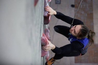 Genç bir kadın hızla tırmanma yarışmasında dikey duvara tırmanıyor, yukarıdan çekilmiş. Kyiv - 6 Mart 2024